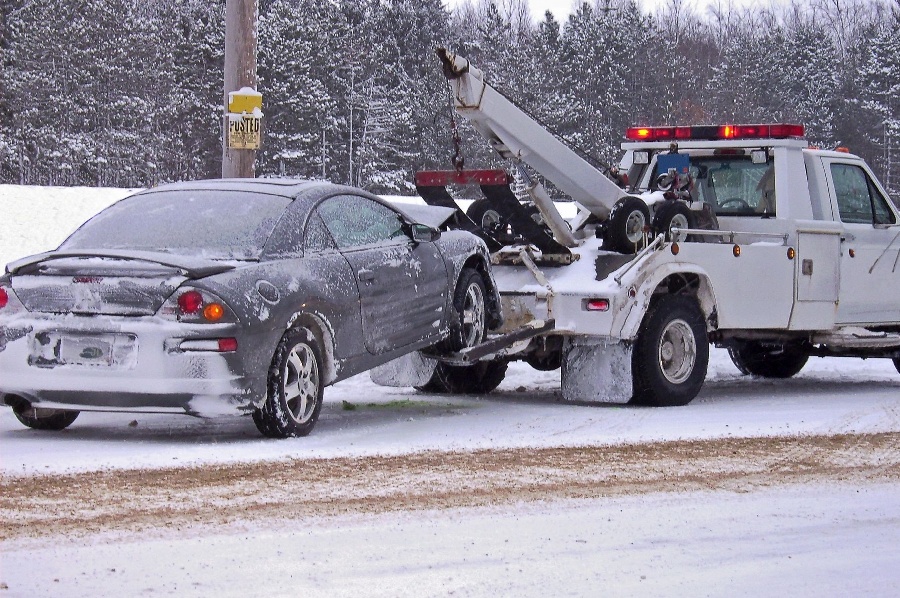 A tow truck towing a car on the side of a road.